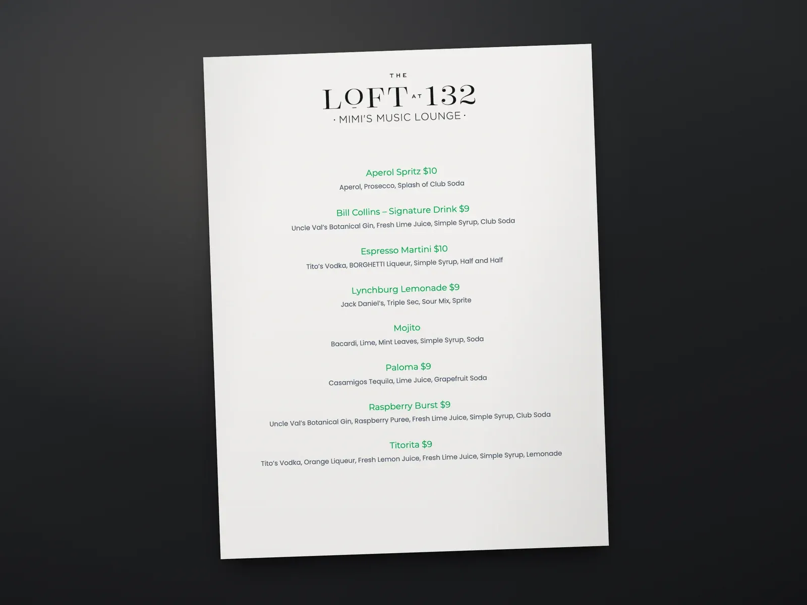 A printed cocktail menu for The Loft at 132 with drink names, ingredients, and prices on a dark table