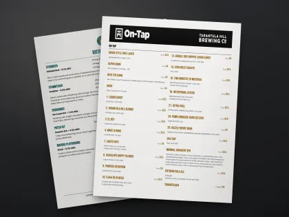 A printed two-column on-tap menu for Tarantula Hill Brewing on a dark table